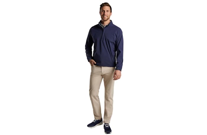 A man wearing a Peter Millar shield half zip rain shell in navy blue.